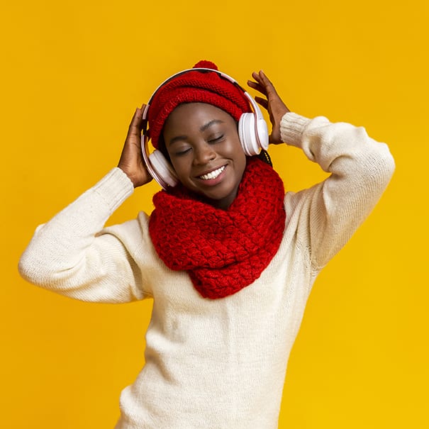 Emotional winter girl listening to music with closed eyes, using wireless headset, yellow background