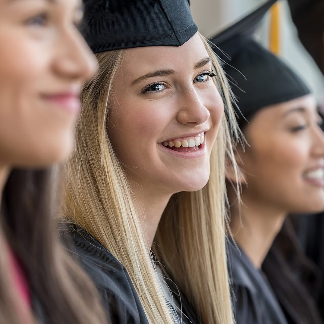 Standing with her fellow graduates, a teen girl smiles with joy at her parents.