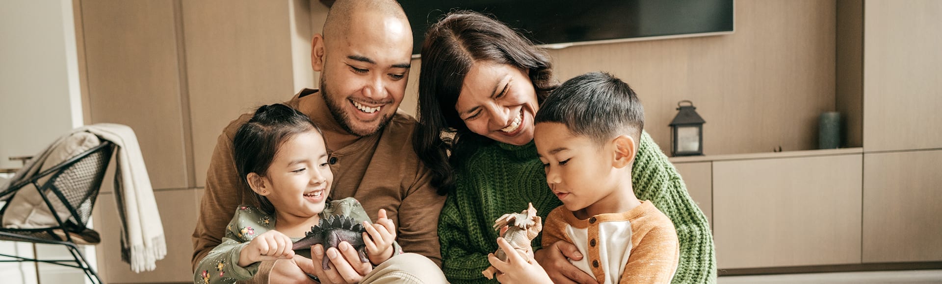 A married couple smiling with their two kids in their laps playing with dinosaur toys